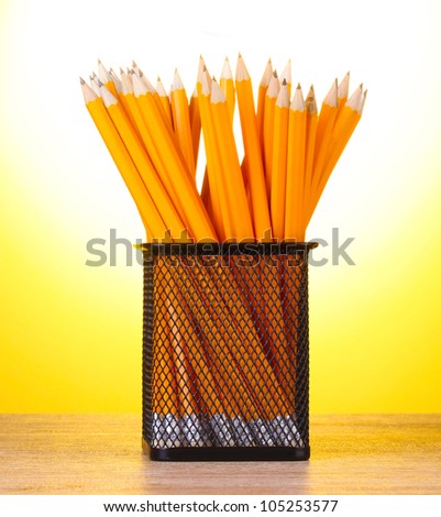 lead pencils in metal cup on wooden table on yellow background