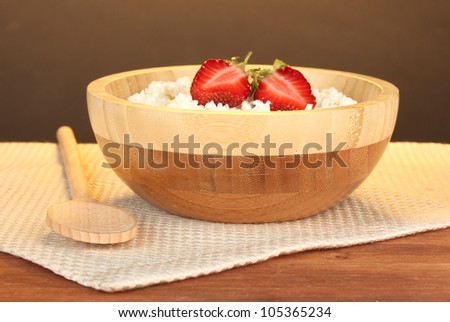 cottage cheese with strawberry in wooden bowl with wooden spoon on beige napkin on wooden table on brown background