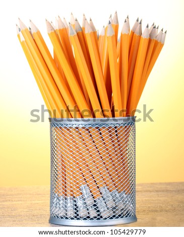 lead pencils in metal cup on wooden table on yellow background