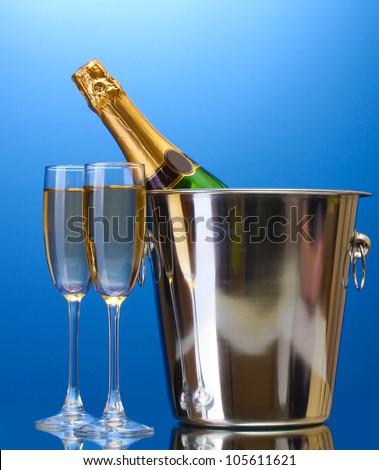 Champagne bottle in bucket with ice and glasses of champagne, on blue background
