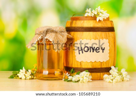 Sweet honey in barrel and jar with flowers on wooden table on green background