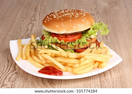 Big and tasty hamburger and fried potatoes on plate on wooden table