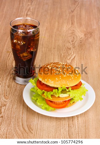 Big and tasty hamburger on plate with cola on wooden table