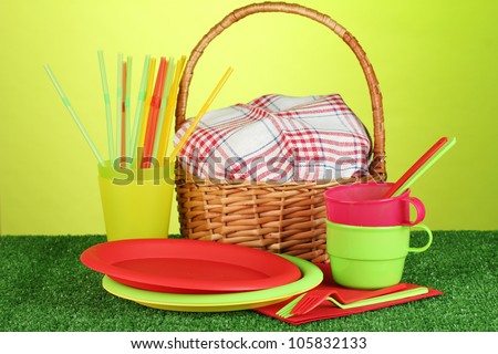 bright plastic disposable tableware and picnic basket on the lawn on colorful background