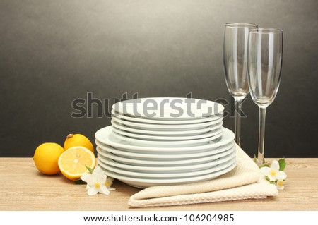 empty clean plates and glasses and lemon on wooden table on grey background
