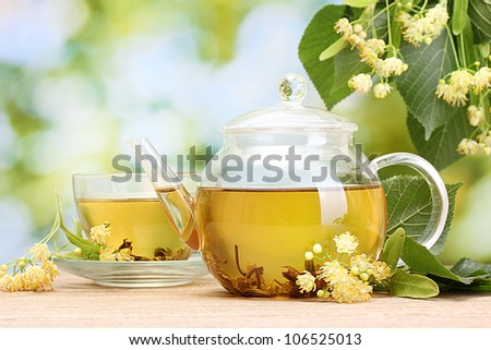 teapot and cup with linden tea  and flowers on wooden table in garden