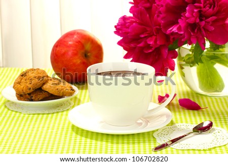 cup hot chocolate, apple, cookies and flowers on table in cafe