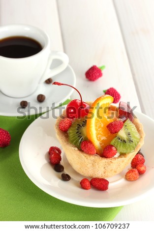 sweet cake with fruits on plate and cup of coffee on wooden table