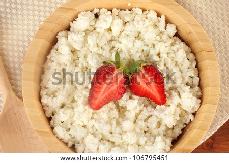 cottage cheese with strawberry in wooden bowl with wooden spoon on beige napkin on wooden table close-up