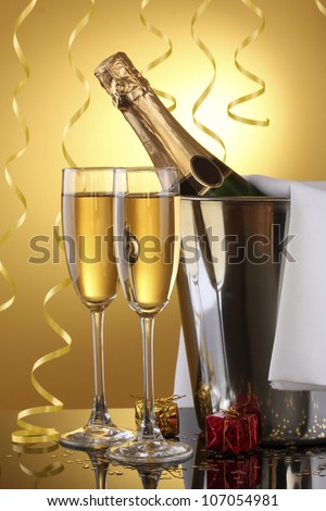 Champagne bottle in bucket with ice and glasses of champagne, on yellow background