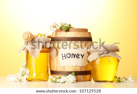 Sweet honey in barrel and jars with acacia flowers on wooden table on yellow background