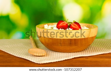 cottage cheese with strawberry in wooden bowl with wooden spoon on beige napkin on wooden table on green background