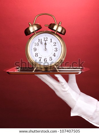 Hand in glove holding silver tray with alarm clock on red background