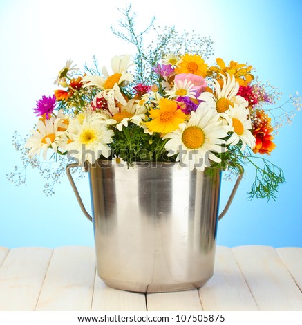 beautiful bouquet of bright  wildflowers in metal bucket, on wooden table on blue background