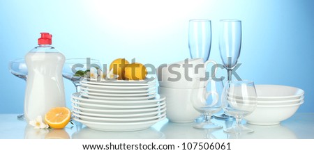 empty clean plates, glasses and cups with dishwashing liquidand lemon on blue background