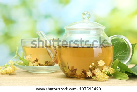 teapot and cup with linden tea  and flowers on wooden table in garden