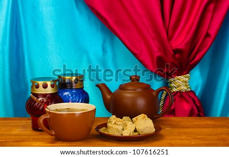 Teapot with cup and saucer with  sweet halva on wooden table on a background of curtain close-up