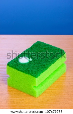 Sponge with dishwashing liquid on wooden table on blue background