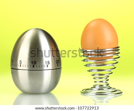 egg timer and egg in metal stand on green background