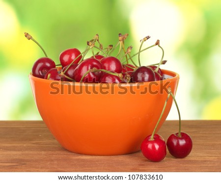 cherry in orange bowl on wooden table on green background