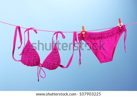 Women\'s swimsuit hanging on a rope on blue background