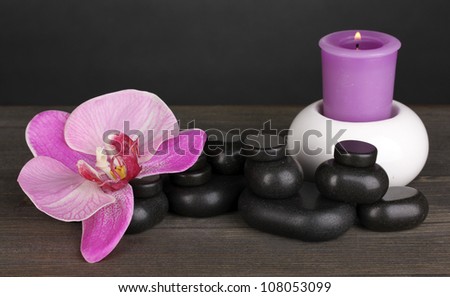 Spa stones with orchid flower and candle on wooden table on grey background