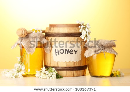 Sweet honey in barrel and jars with acacia flowers on wooden table on yellow background