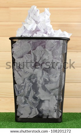 metal trash bin from paper on grass on wooden background