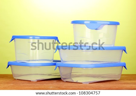 Plastic containers for food on wooden table on green background