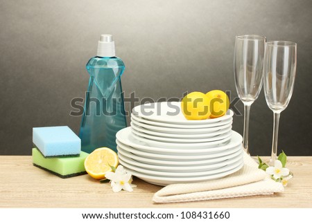 empty clean plates and glasses with dishwashing liquid, sponges and lemon on wooden table on grey background