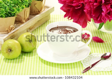 cup hot chocolate, apples and flowers on table in cafe
