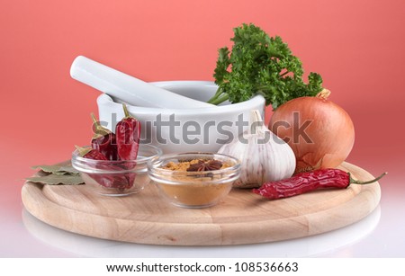 Composition of White mortar and pestle with spice and vegetables on cutting board on red background