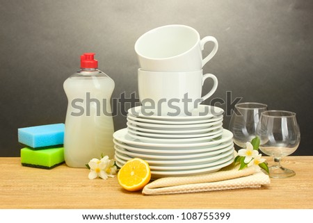 empty clean plates, glasses and cups with dishwashing liquid, sponges and lemon on wooden table on grey background