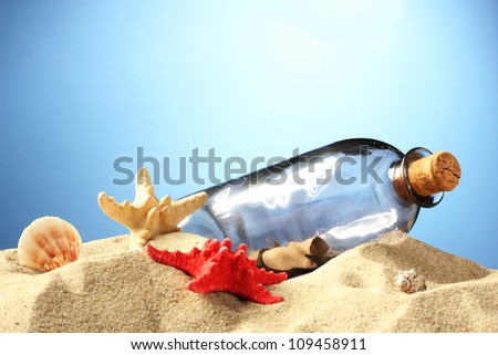Glass bottle with note inside on sand, on blue background