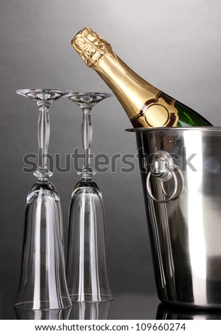 Champagne bottle in bucket with ice and glasses on grey background