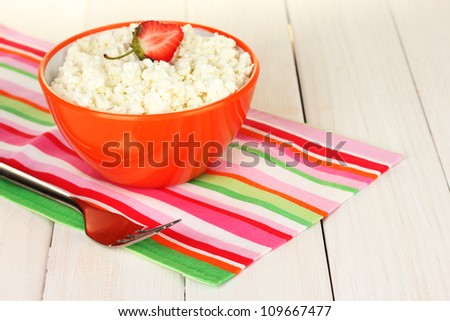 cottage cheese with strawberry in orange bowl and fork on colorful napkin on white wooden table close-up