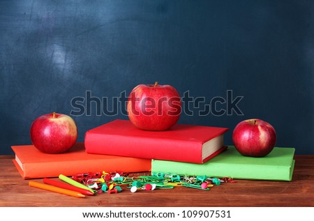 Composition of books, stationery and an apples on the teacher\'s desk in the background of the blackboard