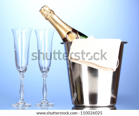 Champagne bottle in bucket with ice and glasses on blue background