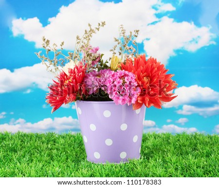 Purple bucket with white polka-dot with flowers on sky background