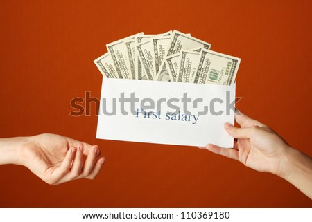 Woman\'s hand passes the envelope with the salary on brown background