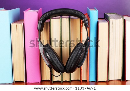 Headphones on books on wooden table on purple background