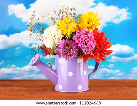 Purple watering can with white polka-dot with flowers on sky background