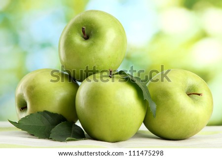 Ripe green apples with leaves, on table, on green background
