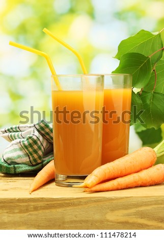 glasses of carrot juice and fresh carrots on wooden table on green background