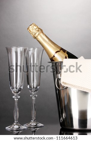 Champagne bottle in bucket with ice and glasses on grey background