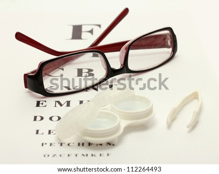glasses, contact lenses in containers and tweezers, on snellen eye chart background