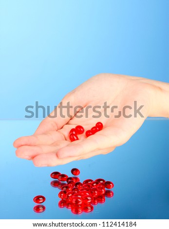 Woman\'s hand holding a red pill on blue background close-up