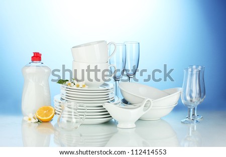empty clean plates, glasses and cups with dishwashing liquid and lemon on blue background