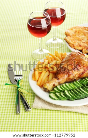 Roast chicken with french fries and cucumbers, glasses of wine on green table cloth