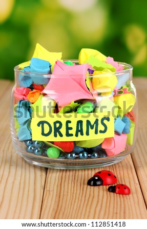 Glass vase with paper stars with dreams on wooden table on natural background